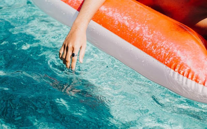 woman dangles her hand in the pool as she floats in an inflatable vessel