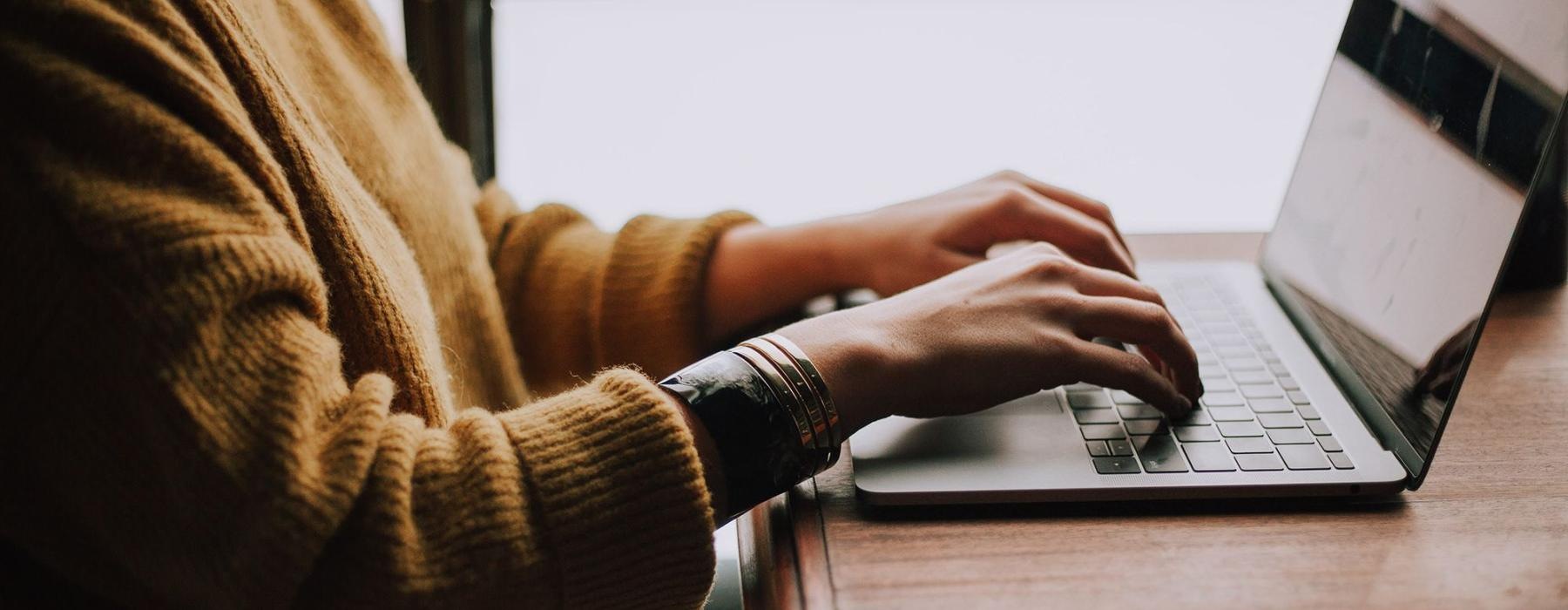 woman types on her laptop near large window